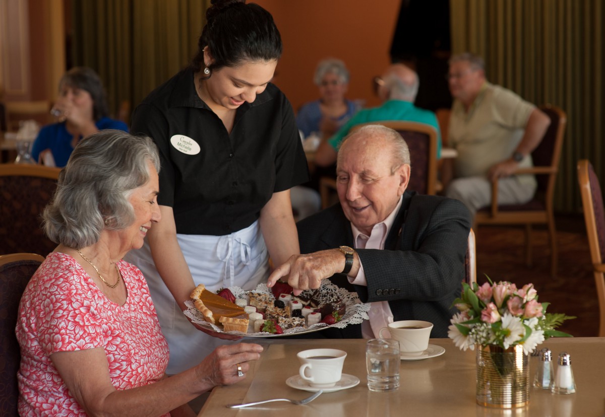 An elderly couple being served by a waitress at a restaurant.