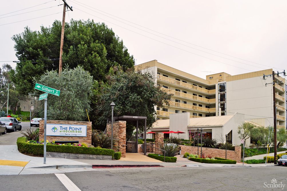 A view of a hotel entrance with surrounding trees and signage on a street corner.