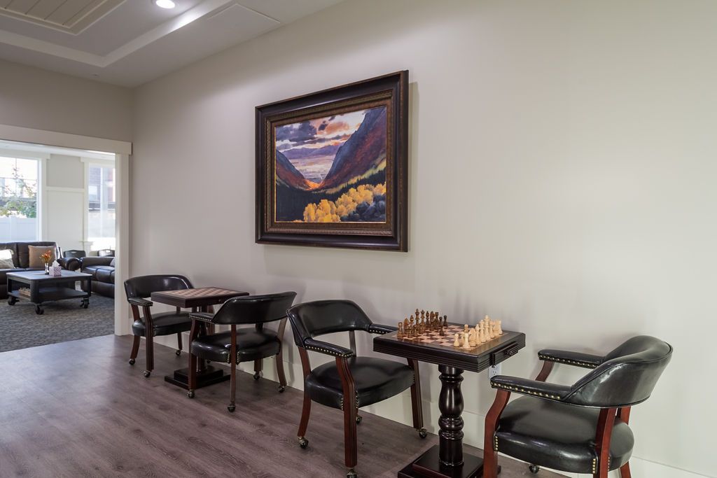 A cozy interior with a chess set on a table, surrounded by chairs and adorned with a colorful painting on the wall.