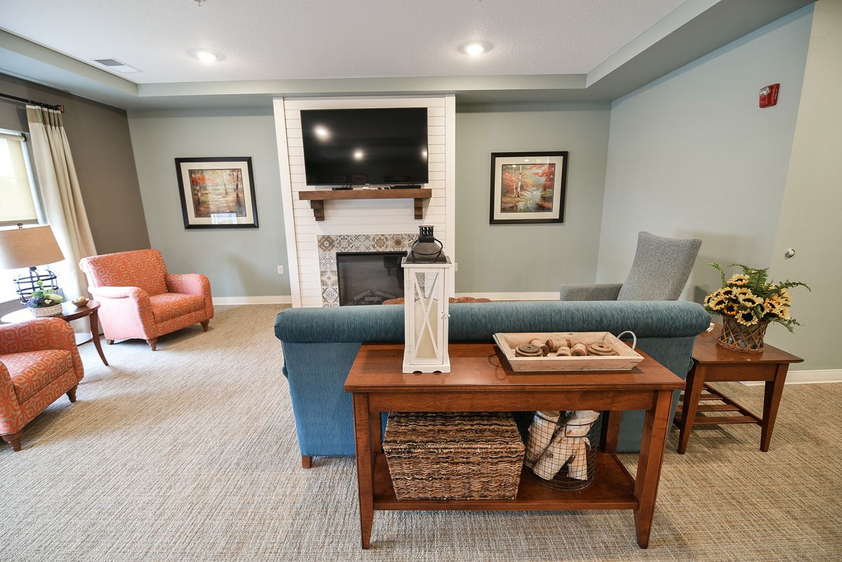 A cozy living room featuring a sofa, armchairs, a television above a fireplace, and decorative elements on a wooden table.