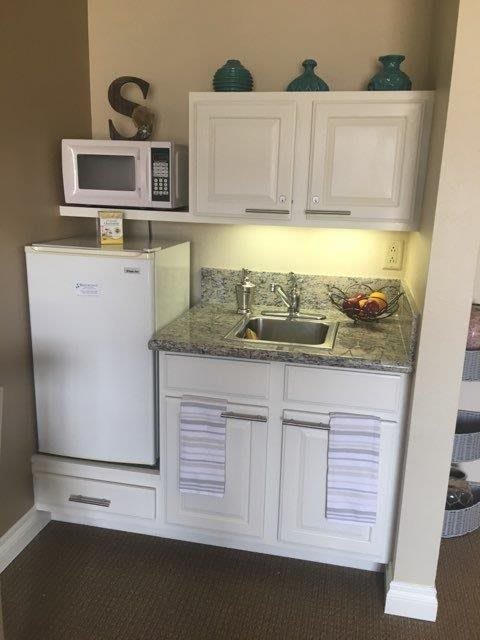 A compact kitchenette with a microwave, mini fridge, sink, and upper and lower cabinets.