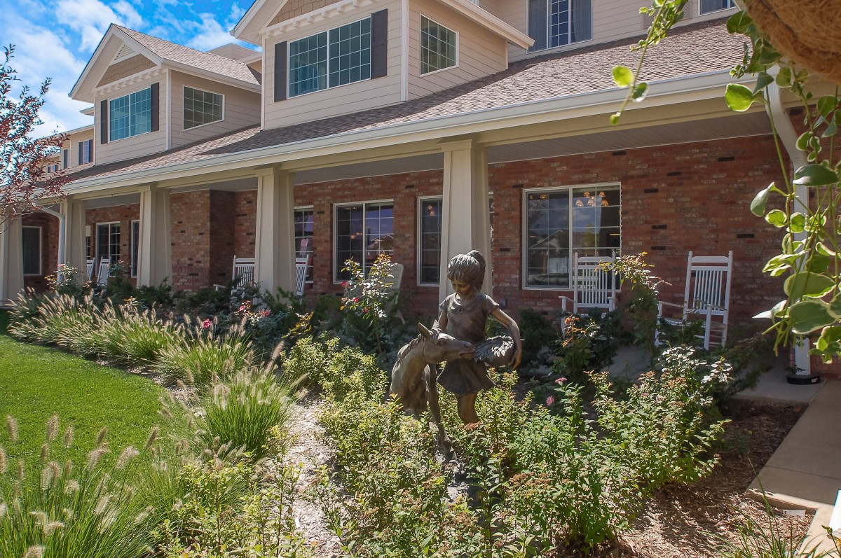 A building with a brick exterior surrounded by lush landscaping and garden statues.