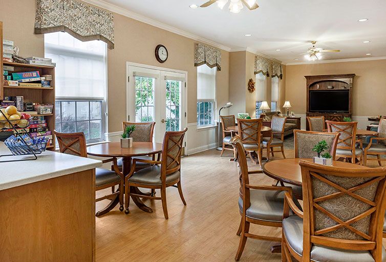 A cozy dining area with several wooden tables and chairs, featuring large windows and natural lighting.