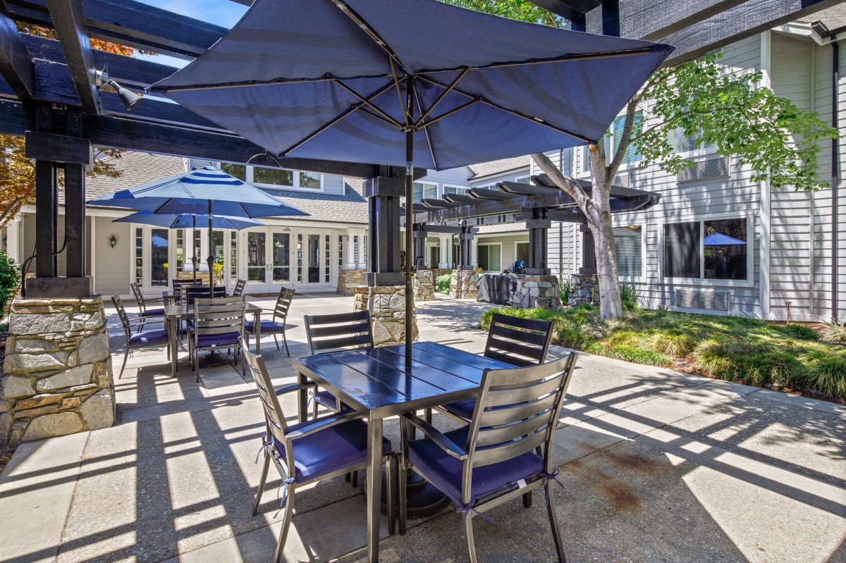 A cozy outdoor patio with tables, chairs, and large umbrellas providing shade.