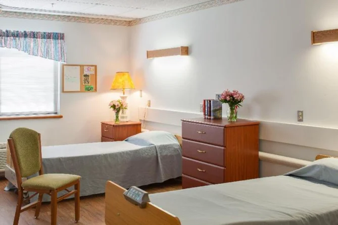 A tidy hospital room with two single beds, wooden furniture, and decorative flowers.