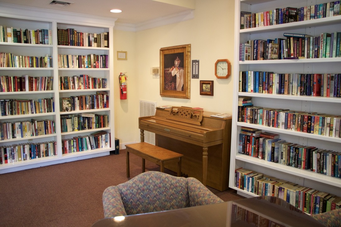A cozy library corner featuring bookshelves filled with books, a piano, and comfortable seating.