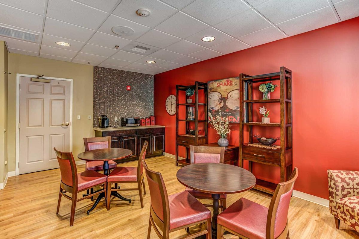 A cozy indoor lounge area with tables and chairs, featuring a red accent wall and decorative bookshelves.