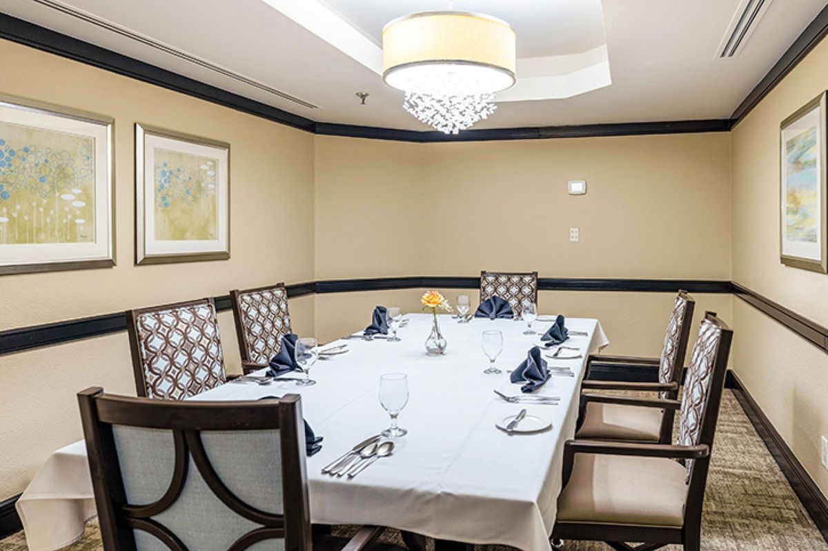 An elegantly set dining table in a private room with cushioned chairs and a chandelier overhead.