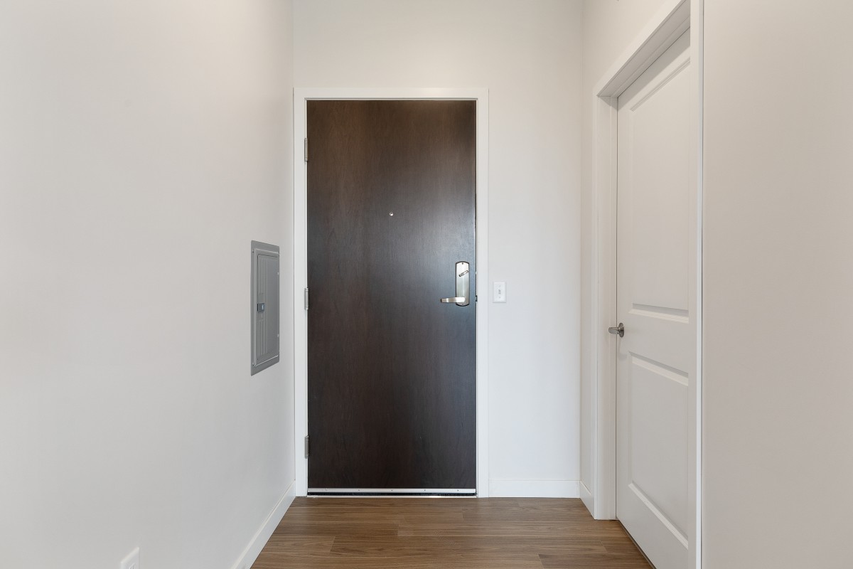 A simple hallway with a wooden door, white walls, and wood flooring.