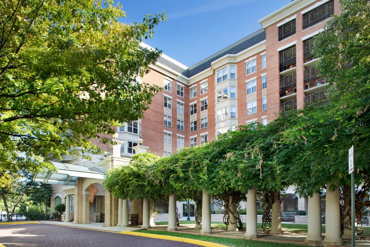 A modern apartment building with lush trees in the foreground on a sunny day.