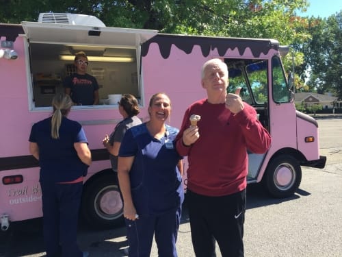 A group of people enjoying ice cream outside a pink ice cream truck on a sunny day.