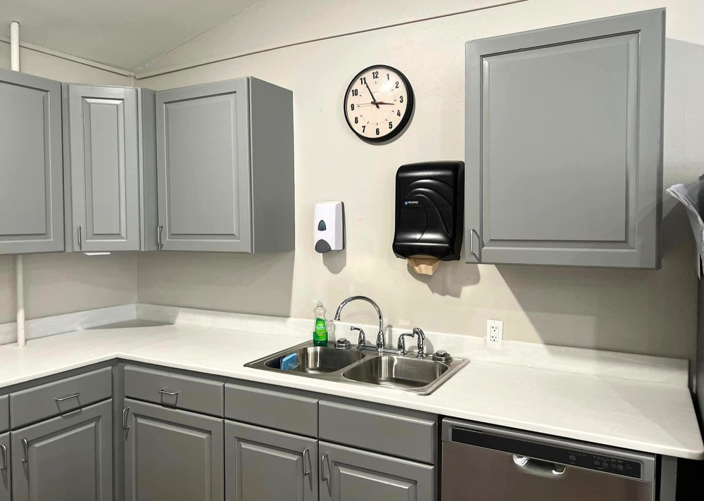 A clean, modern kitchen with gray cabinets, a sink, and wall-mounted clock.