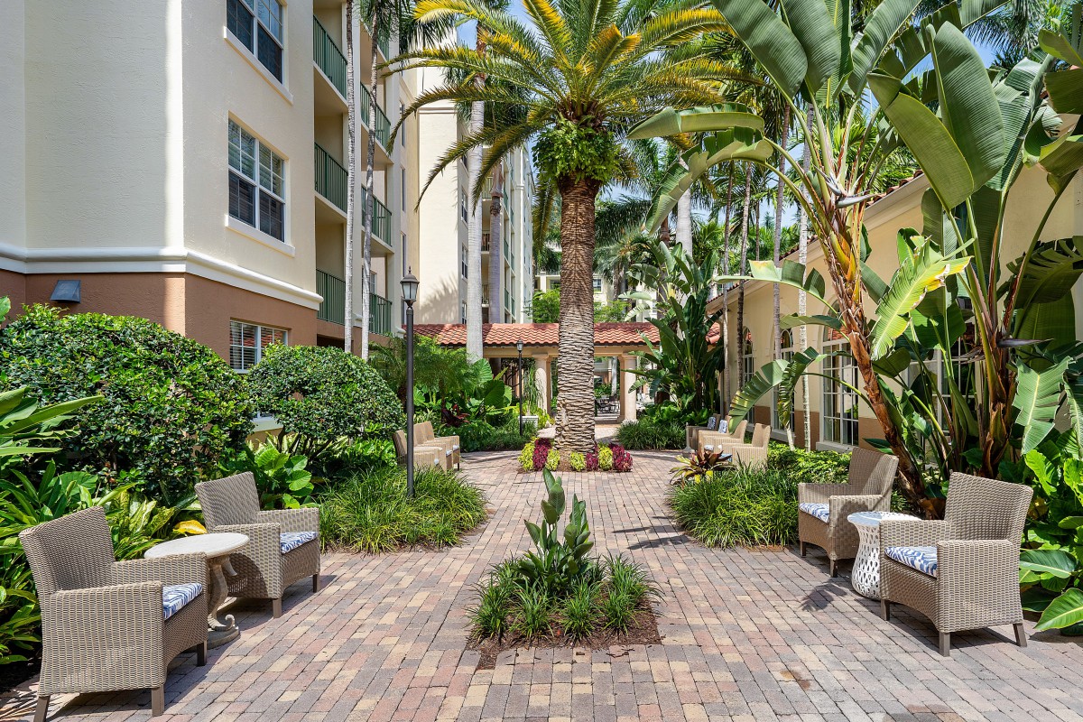 A serene courtyard with lush palm trees and comfortable outdoor seating at an apartment complex.