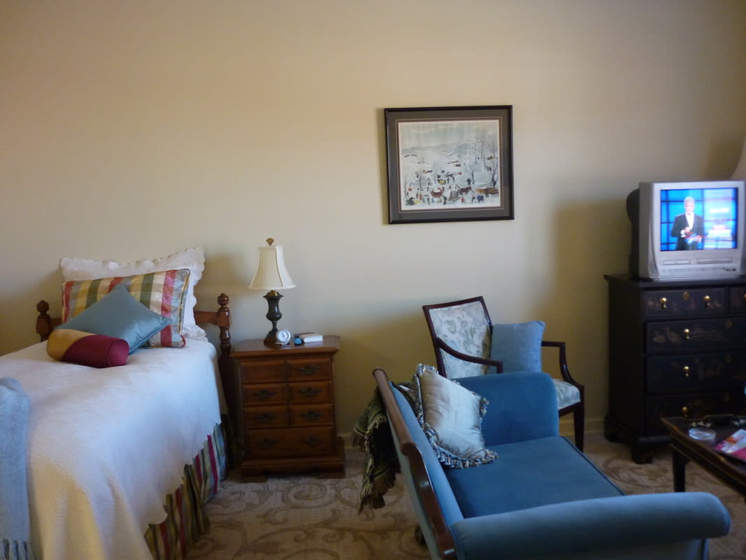 A cozy bedroom with a bed, chair, and television.