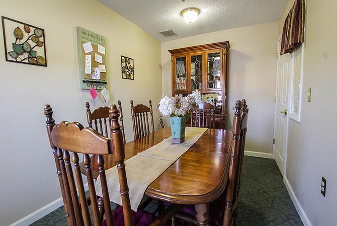 A cozy dining room with a wooden table and chairs, decorated with a vase of flowers and a table runner.