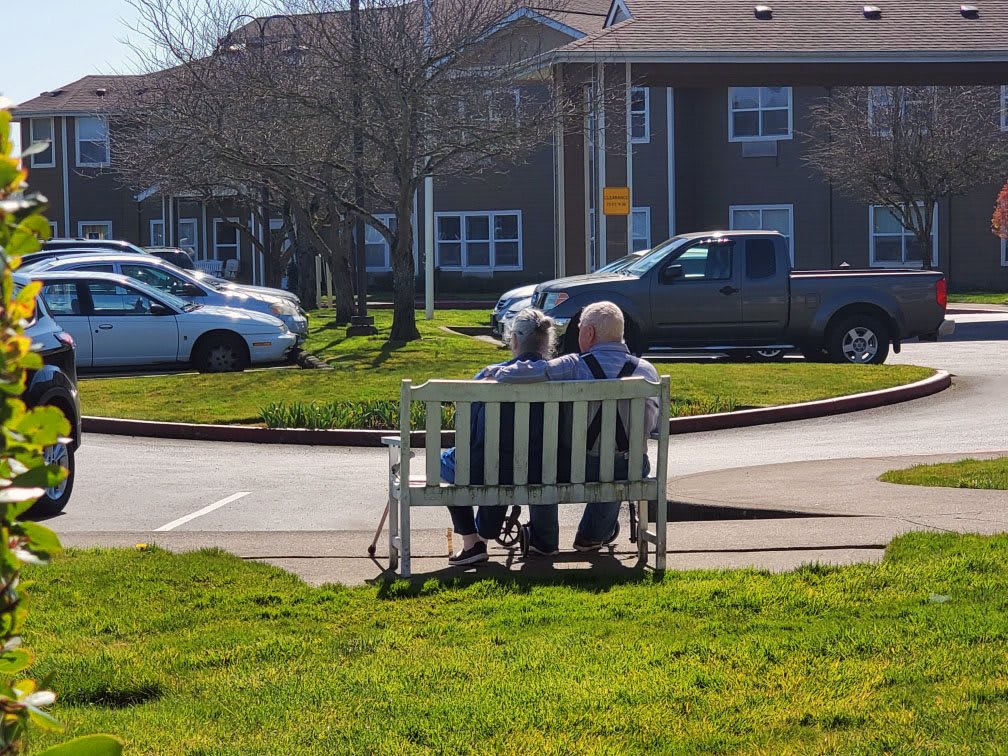 An elderly couple sitting together on a bench enjoying a sunny day.