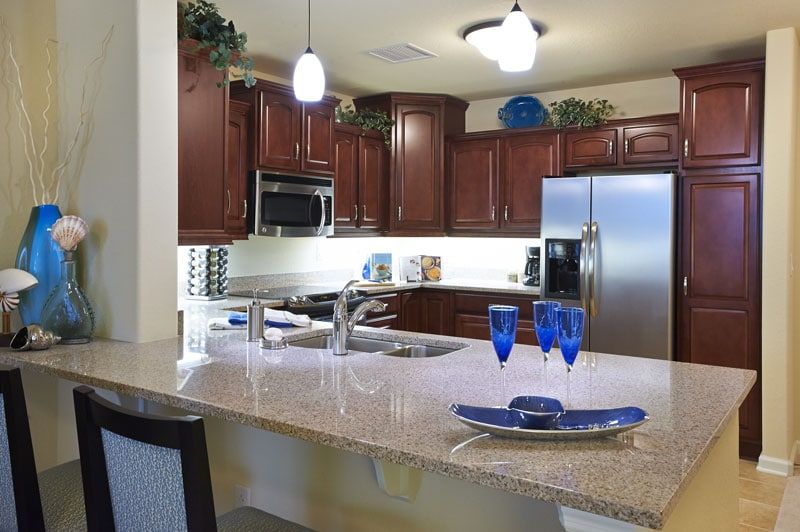 A modern kitchen with cherry wood cabinets, stainless steel appliances, and a granite countertop adorned with blue glassware.