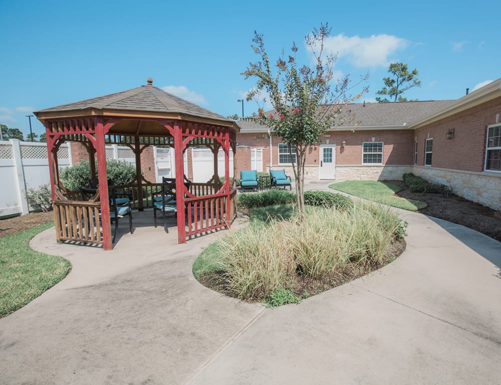 A serene outdoor space featuring a red gazebo, surrounded by landscaped gardens and a pathway.