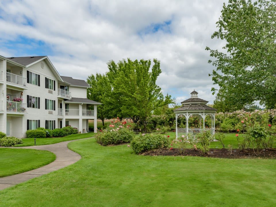 A picturesque garden with a gazebo and a pathway leading to a large house.