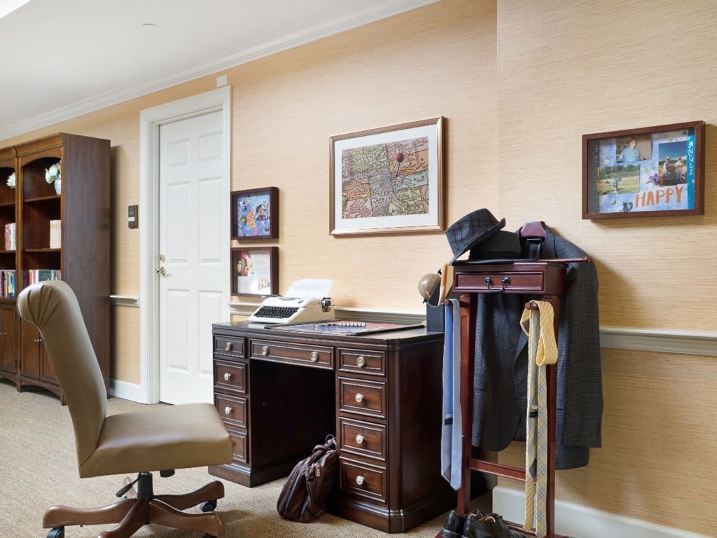 A cozy home office setup featuring a wooden desk with a typewriter, a chair, and a clothing rack with garments.
