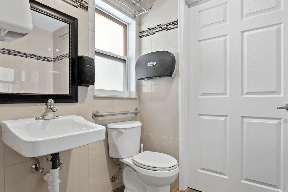 A clean and modern bathroom with a sink, toilet, mirror, and paper towel dispenser.