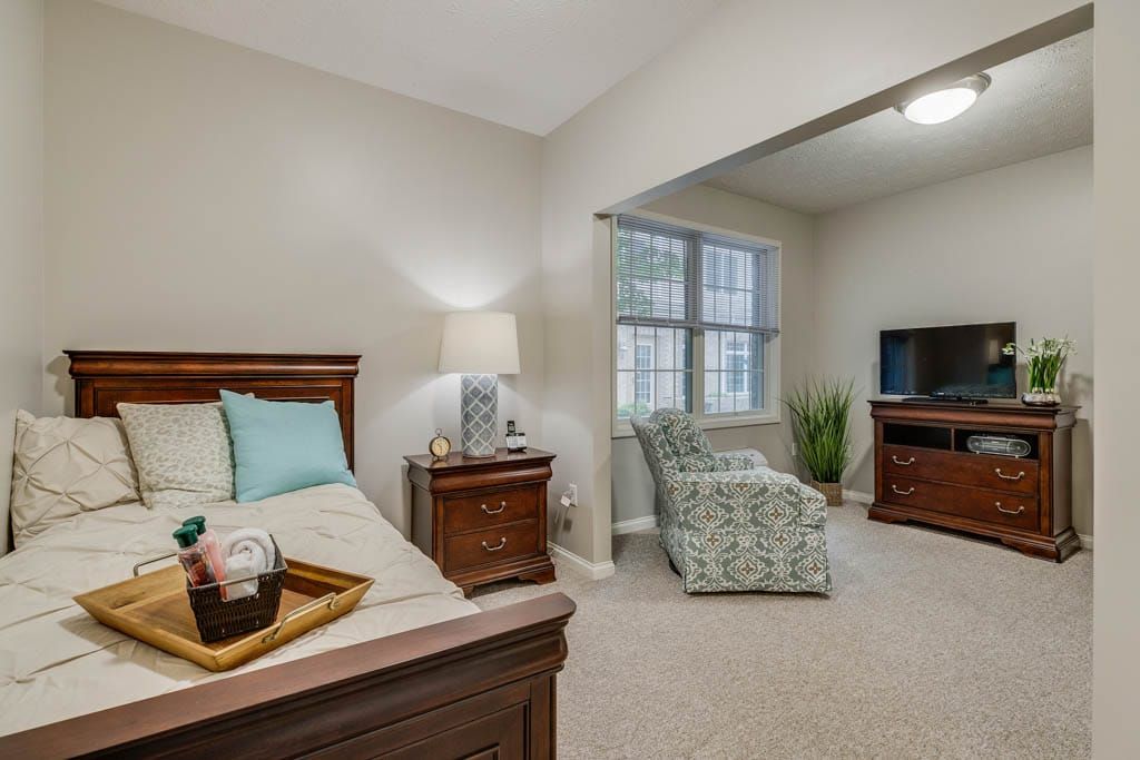 A cozy bedroom with a bed, lamp, armchair, and TV.