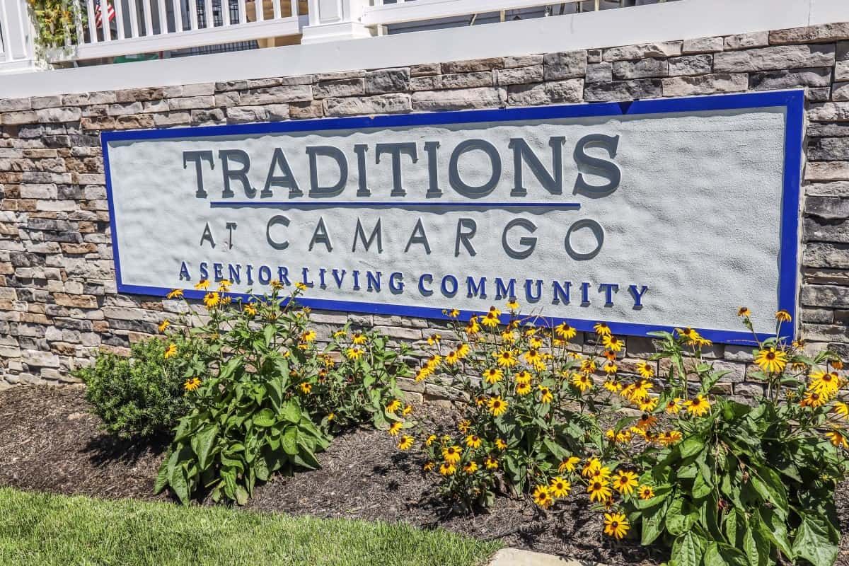 Sign for Traditions at Camargo, a senior living community, surrounded by flowers.