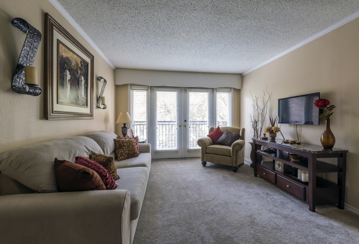 A cozy living room with neutral tones, featuring a sofa, armchair, and TV setup.