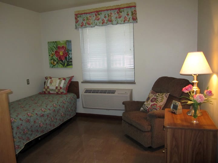 A cozy bedroom with a bed, armchair, and a side table with a lamp.