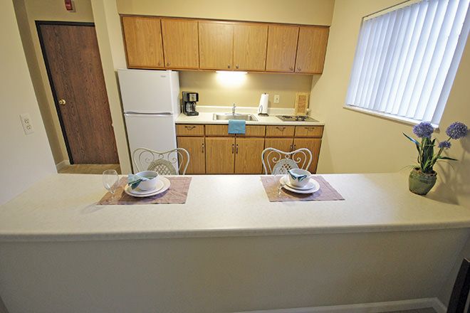 A compact kitchen with a breakfast counter set for two, featuring wooden cabinets and a window providing natural light.