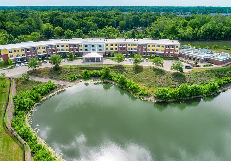Aerial view of a building surrounded by lush greenery and a tranquil lake.