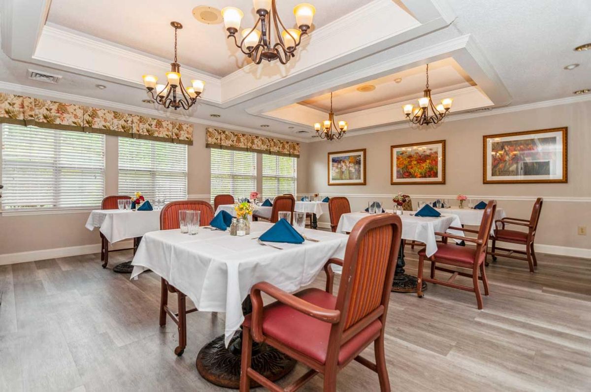 A well-arranged dining room with elegantly set tables, cushioned chairs, and decorative chandeliers.
