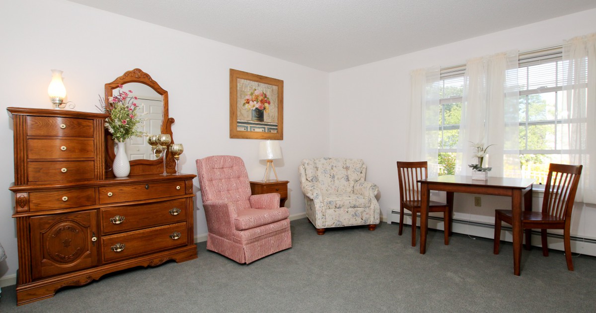 A cozy living room with vintage furniture, including an armchair, a dresser, and a dining table set.