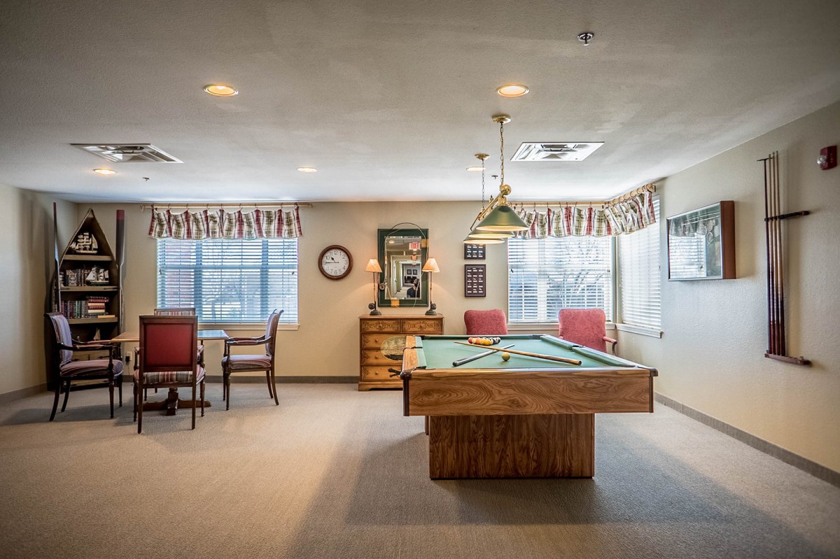 A well-lit game room featuring a billiard table and seating area.