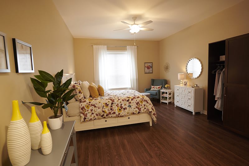 A cozy bedroom with warm lighting, featuring a floral bedspread, wooden flooring, and elegant decor.