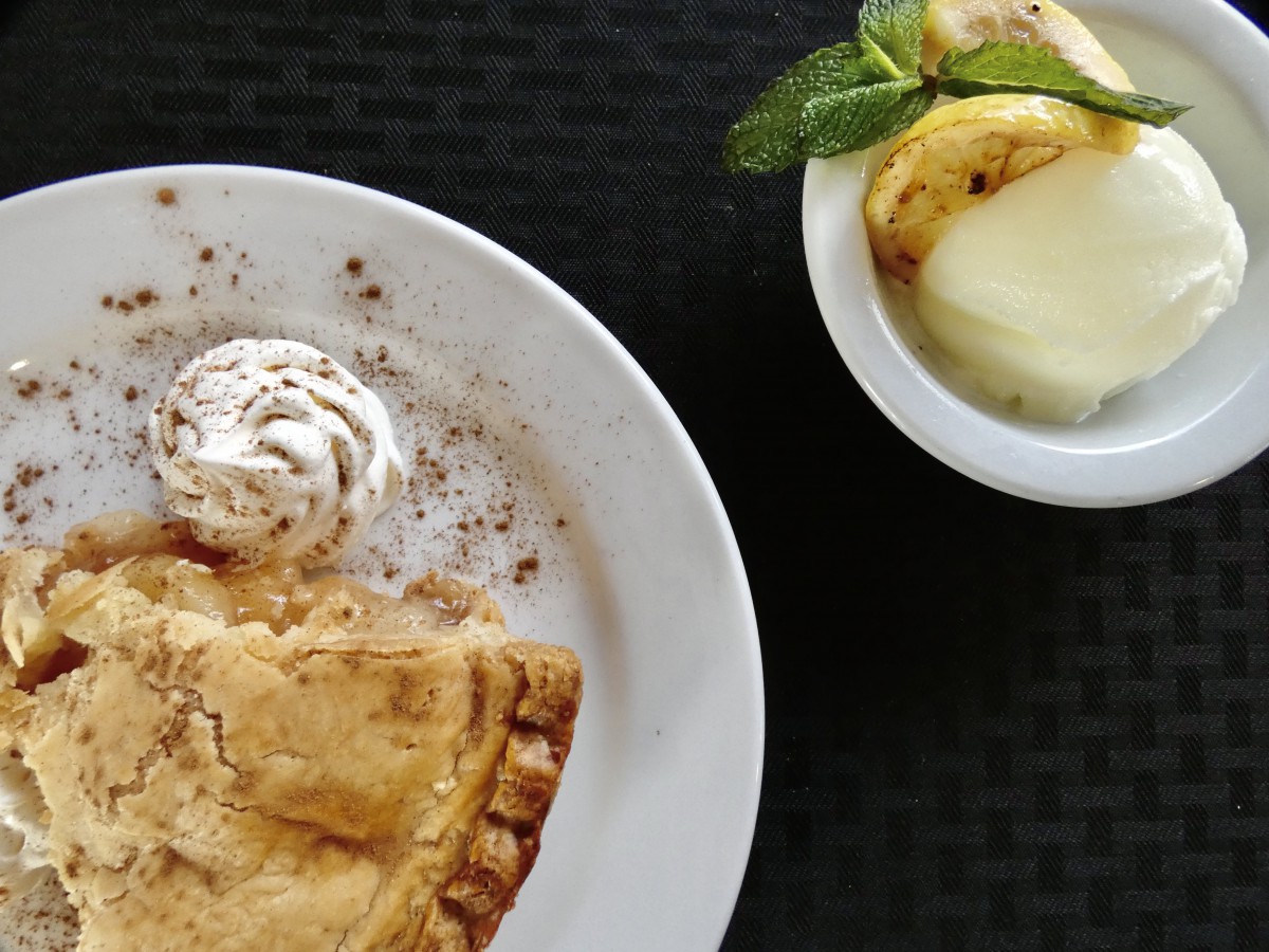 A delicious slice of pie with a dollop of whipped cream, accompanied by a fruit bowl garnished with mint.