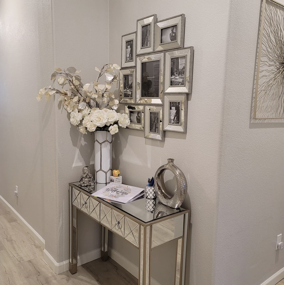 A stylish hallway with a mirrored console table adorned with flowers and framed photos.