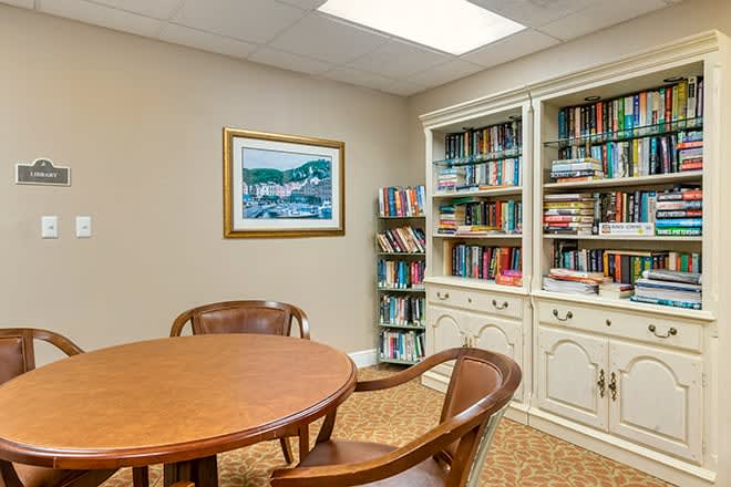 A cozy reading room with bookshelves and a round wooden table surrounded by chairs.