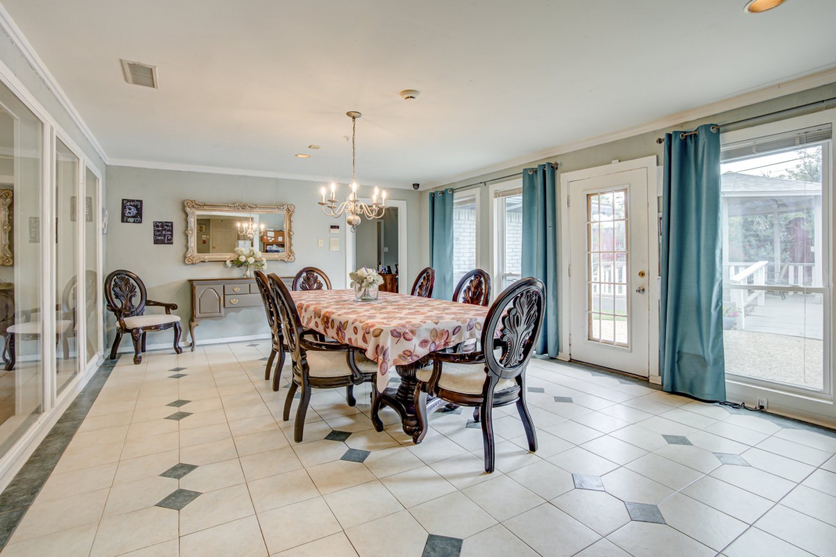 A spacious dining room with a large table, elegant chairs, and a chandelier overhead.
