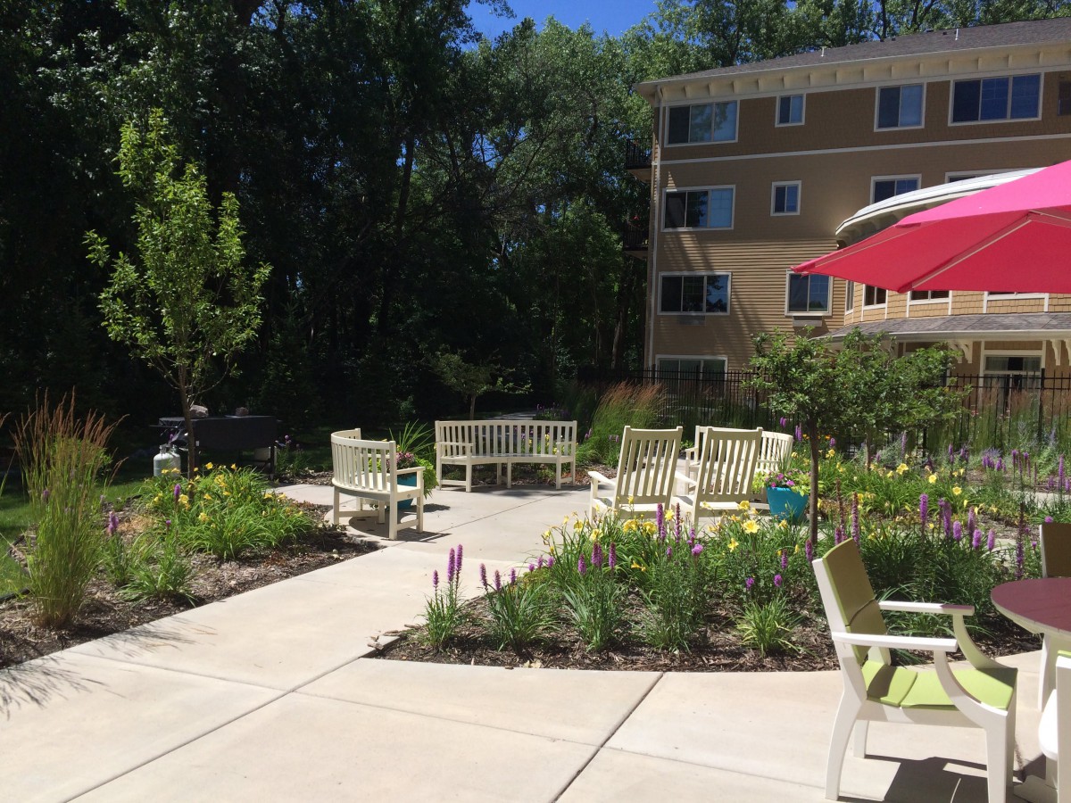 A sunny patio area with seating and gardens in front of a residential building.