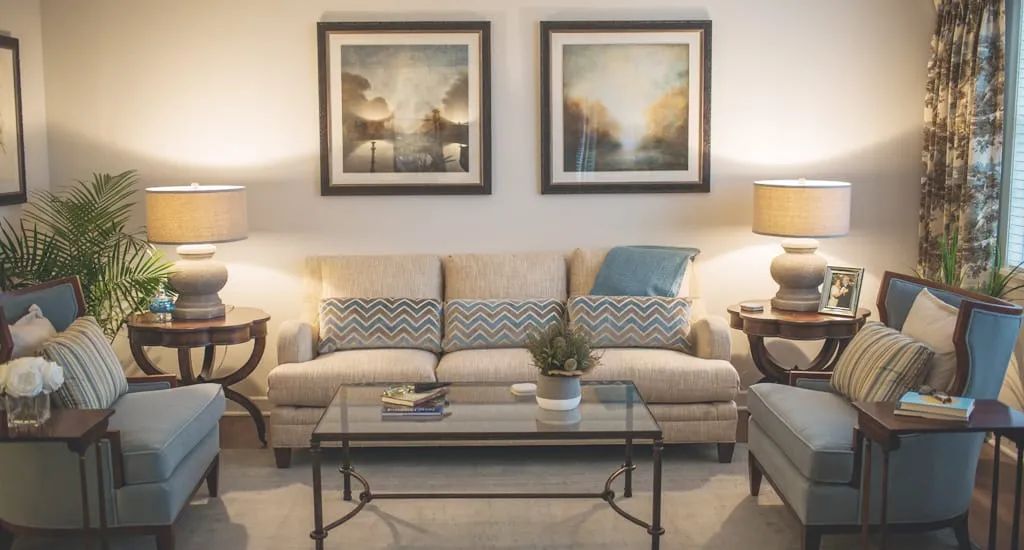 A cozy living room featuring a beige sofa, glass coffee table, and framed artwork on the wall.