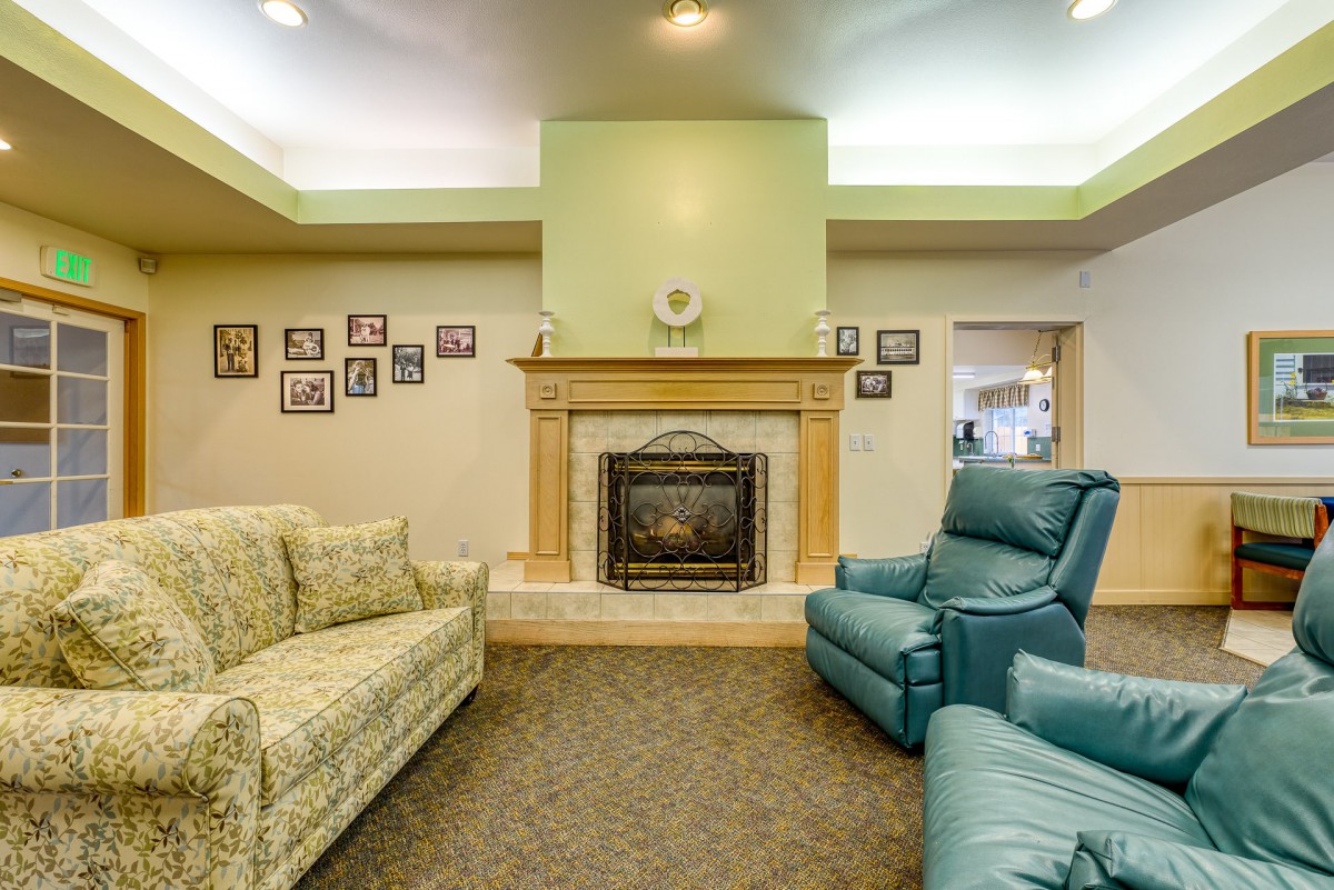 A cozy living room featuring a fireplace, floral-patterned couch, and armchair with family photos adorning the walls.