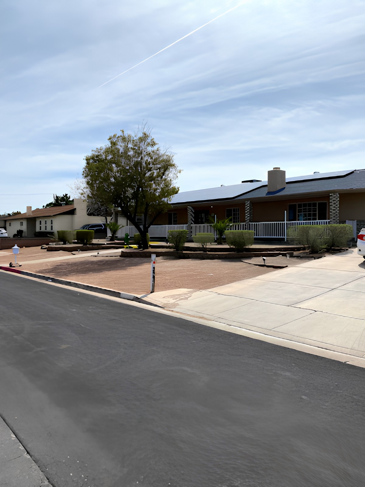 A suburban street with houses, driveways, and a sidewalk under a clear sky.