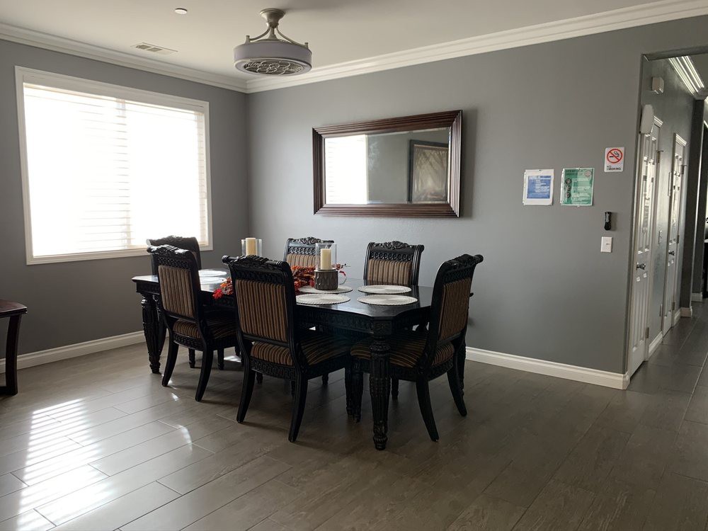 A dining room featuring a dark wooden table with six chairs, a large mirror on the wall, and a chandelier overhead.