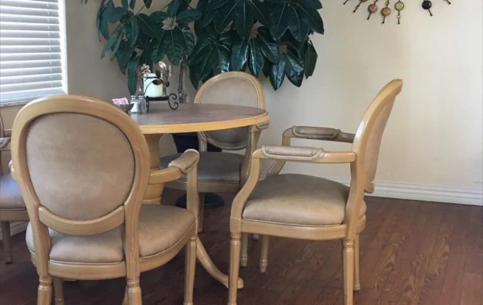 A cozy dining area with a round table and four upholstered chairs, surrounded by indoor plants.
