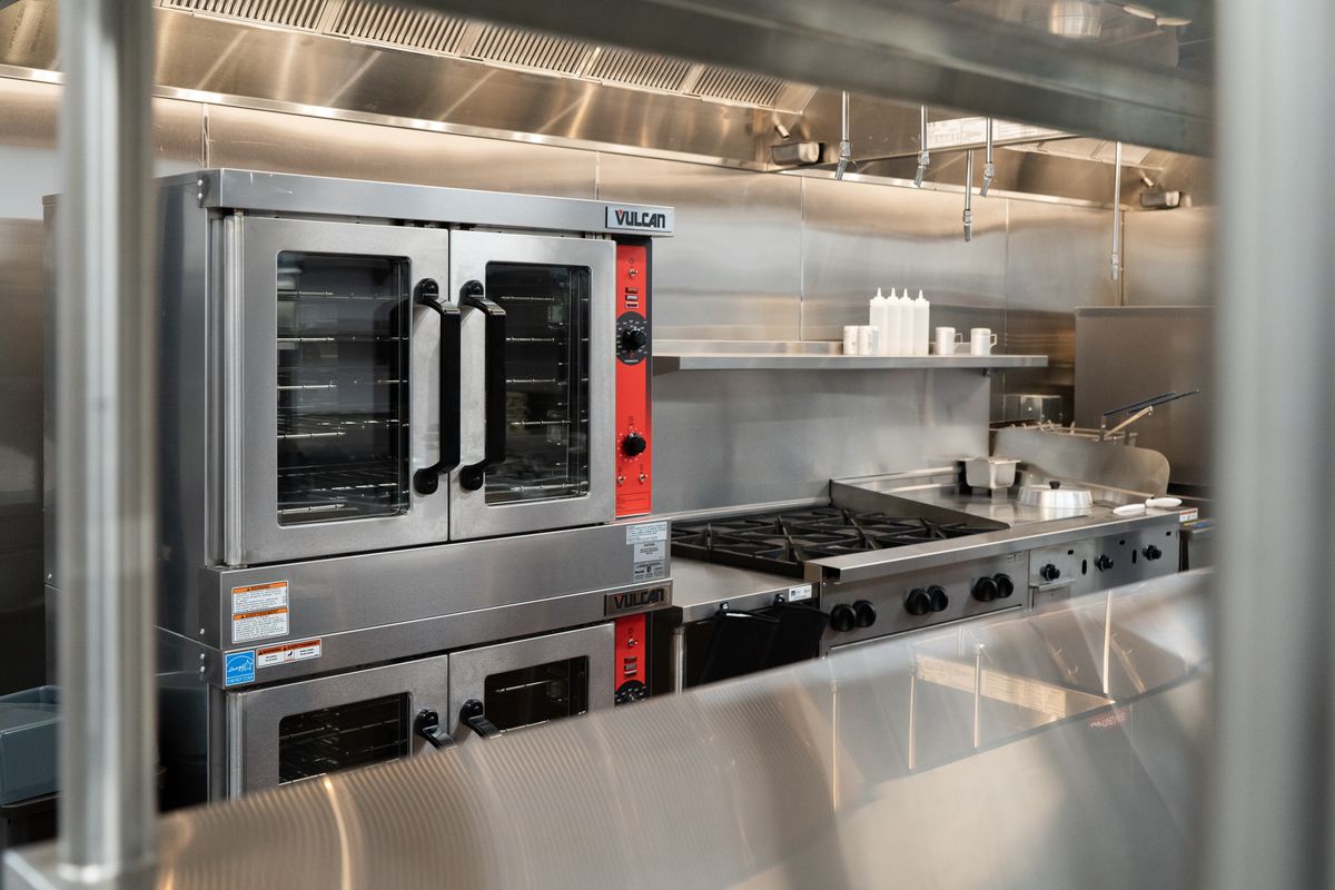 A modern commercial kitchen featuring stainless steel equipment including an oven and stovetop.