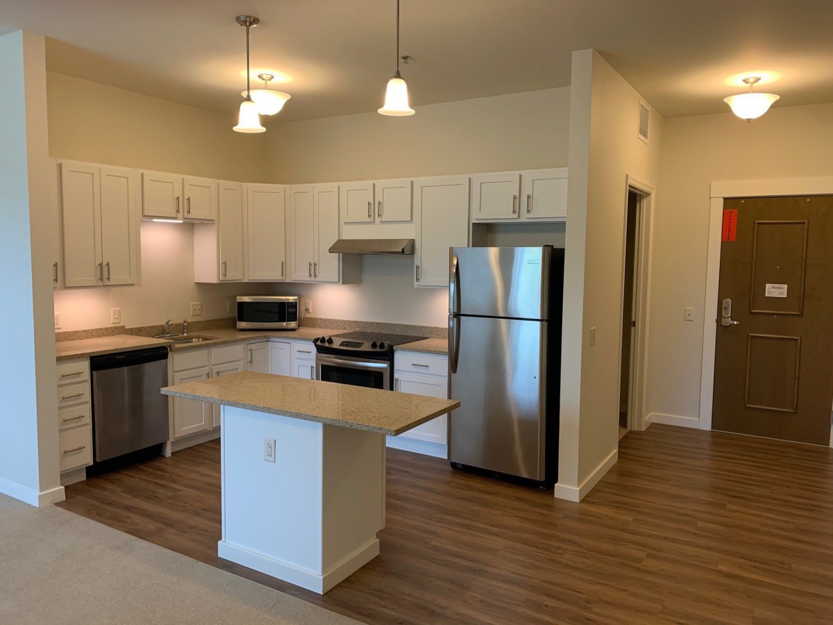 A modern apartment kitchen with stainless steel appliances and an open layout featuring an island and white cabinets.