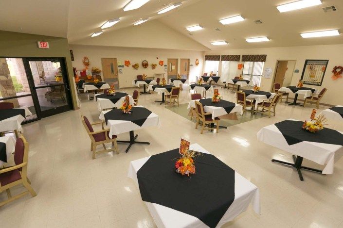 An indoor dining area with tables and chairs arranged, each table adorned with black tablecloths and fall-themed decorations.