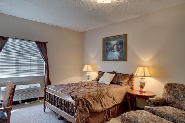 A cozy bedroom with a neatly made bed, lamps on nightstands, and a large window with curtains.