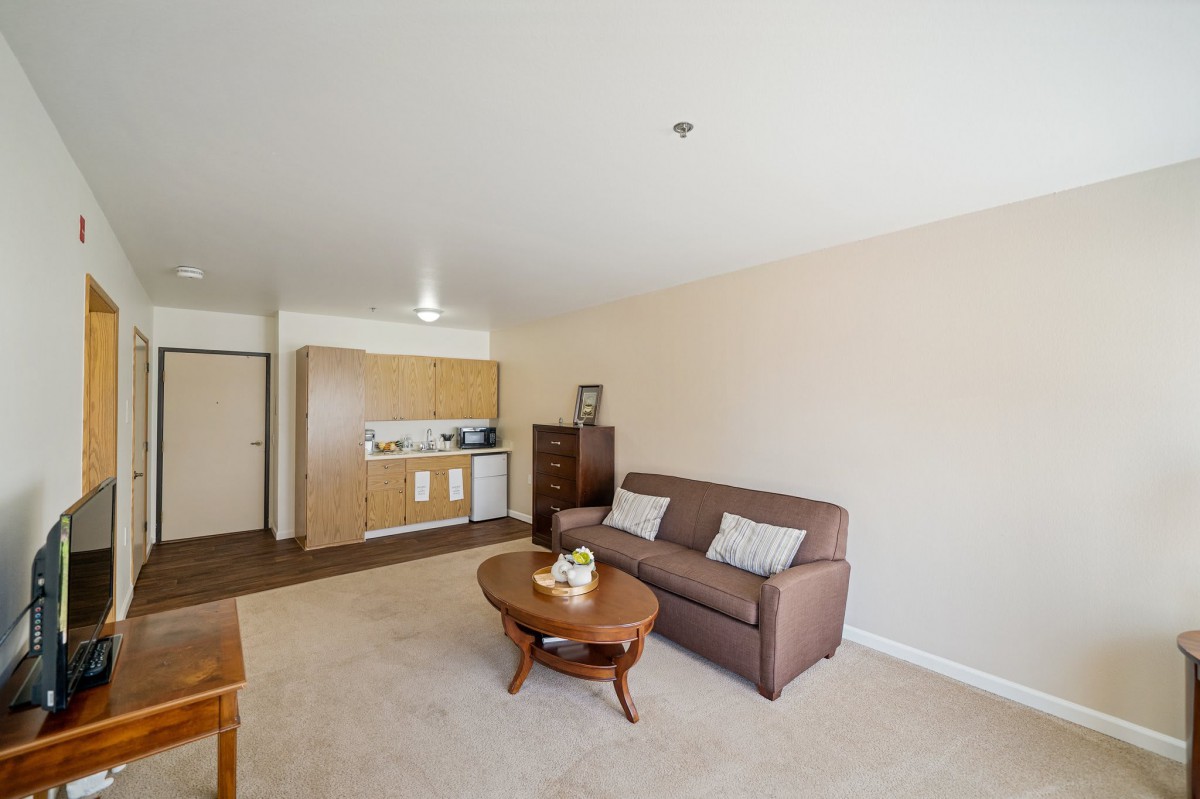 A cozy apartment living room with a sofa, coffee table, and kitchenette in the background.